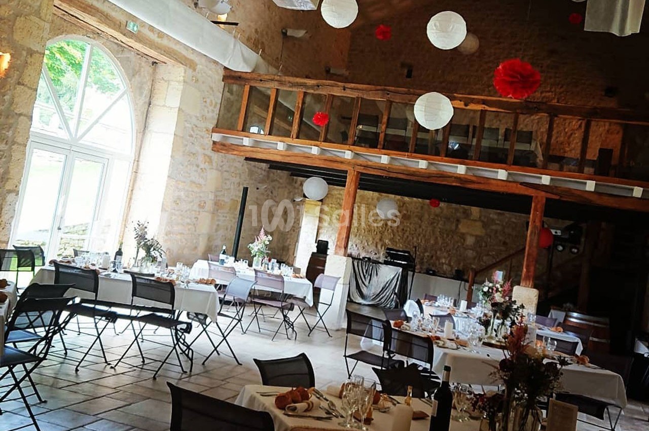 Salle de réception en pierre avec tables dressées, décorations suspendues et mezzanine en bois.
