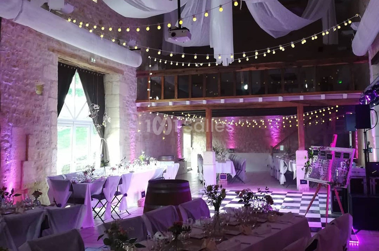 Salle de réception décorée avec des guirlandes lumineuses, des nappes blanches et une ambiance lumineuse violette.