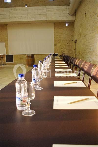 Table de réunion longue avec chaises alignées, bouteilles d'eau, verres, blocs-notes et crayons dans une salle en pierre.