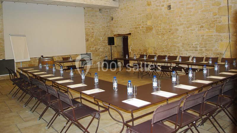Salle de réunion en configuration en U avec tables, chaises, bouteilles d'eau, blocs-notes et écran de projection.