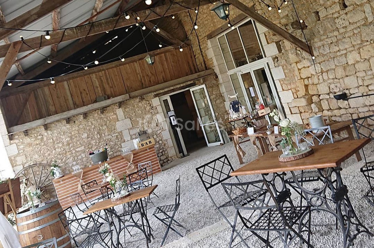 Espace extérieur couvert avec tables et chaises en métal, décoré de guirlandes lumineuses et plantes sur fond de murs en…