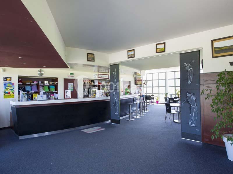 Intérieur d'un bar avec comptoirs modernes, tables et chaises, décorations murales et grande baie vitrée.