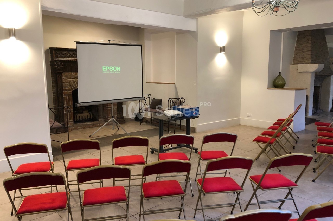 Salle de réunion avec des chaises rouges alignées, un projecteur Epson et un écran de projection.