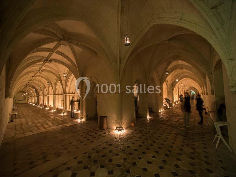 Vue d'une galerie voûtée éclairée par des lumières tamisées, avec quelques silhouettes de visiteurs.