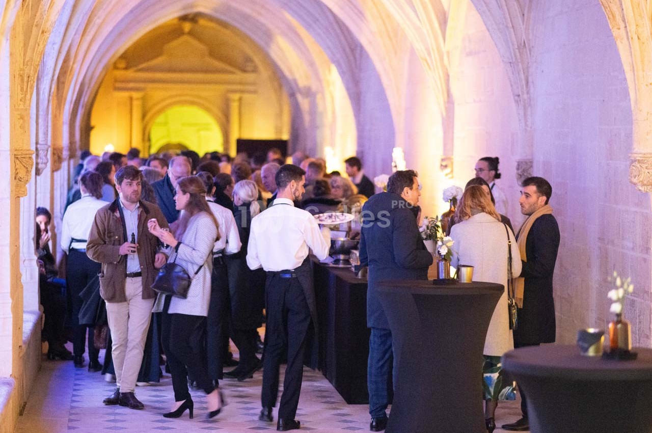 Des personnes discutent et se restaurent dans une galerie voûtée éclairée, lors d'un événement convivial.