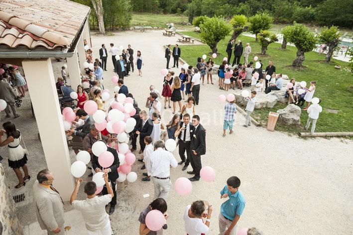 Groupe de personnes rassemblées en extérieur, tenant des ballons roses et blancs, dans une ambiance festive.