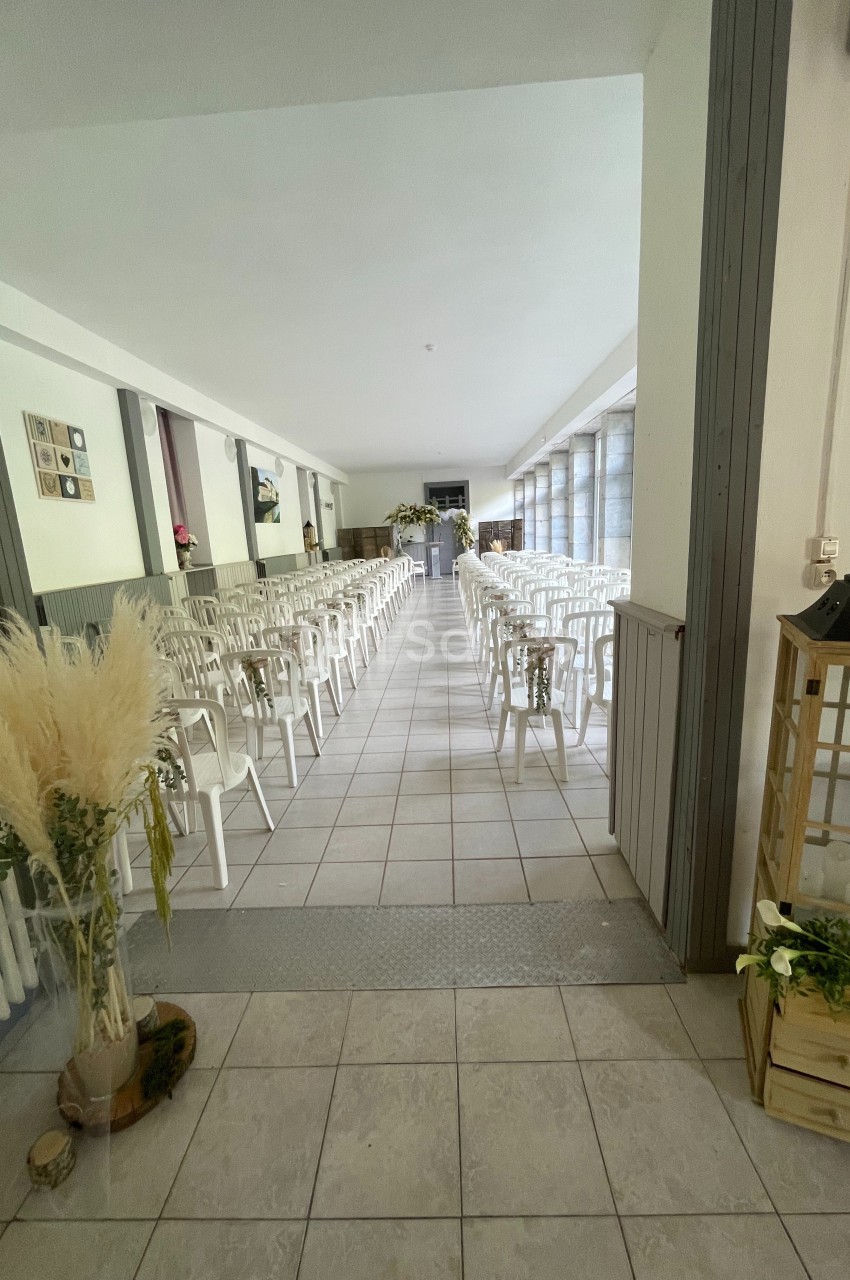 Salle lumineuse aménagée avec des rangées de chaises blanches alignées pour un événement ou une cérémonie.