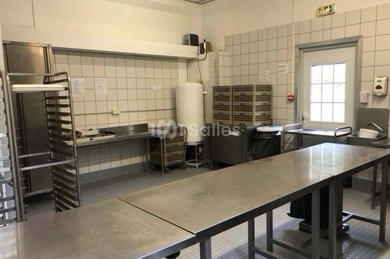 Cuisine professionnelle avec plans de travail en inox, étagères, chariots et équipements de rangement.