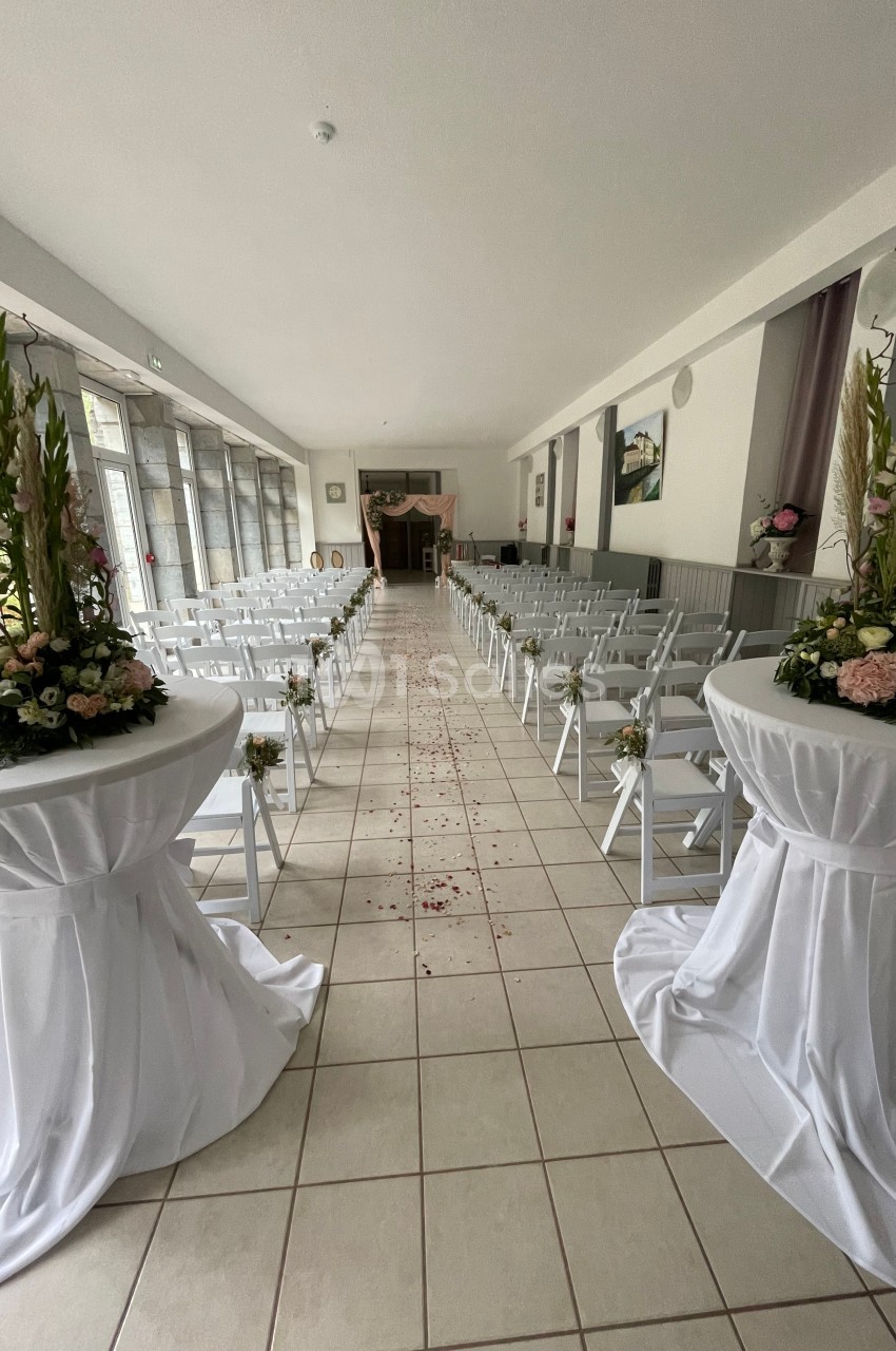 Allée centrale décorée pour une cérémonie, entourée de chaises blanches et de compositions florales.