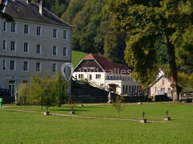 Bâtiment nommé ’L'Orangerie’ entouré d'espaces verts, avec des arbres et des collines en arrière-plan.