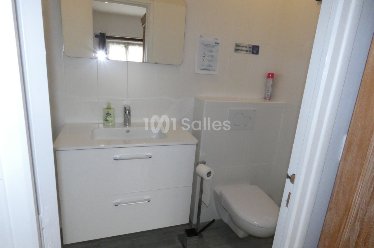 Salle de bain avec lavabo, miroir, toilettes suspendues, papier toilette et sol en carrelage gris.