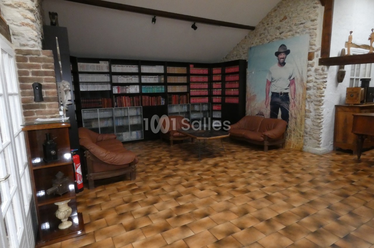 Bibliothèque murale avec livres colorés, fauteuils en cuir, table basse et grande affiche d'un homme en tenue de cowboy.