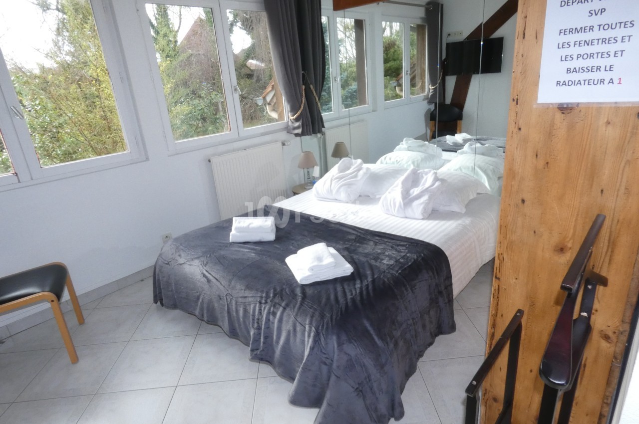Chambre lumineuse avec lit double, draps blancs, couverture grise, grandes fenêtres et panneau d'instructions au mur.