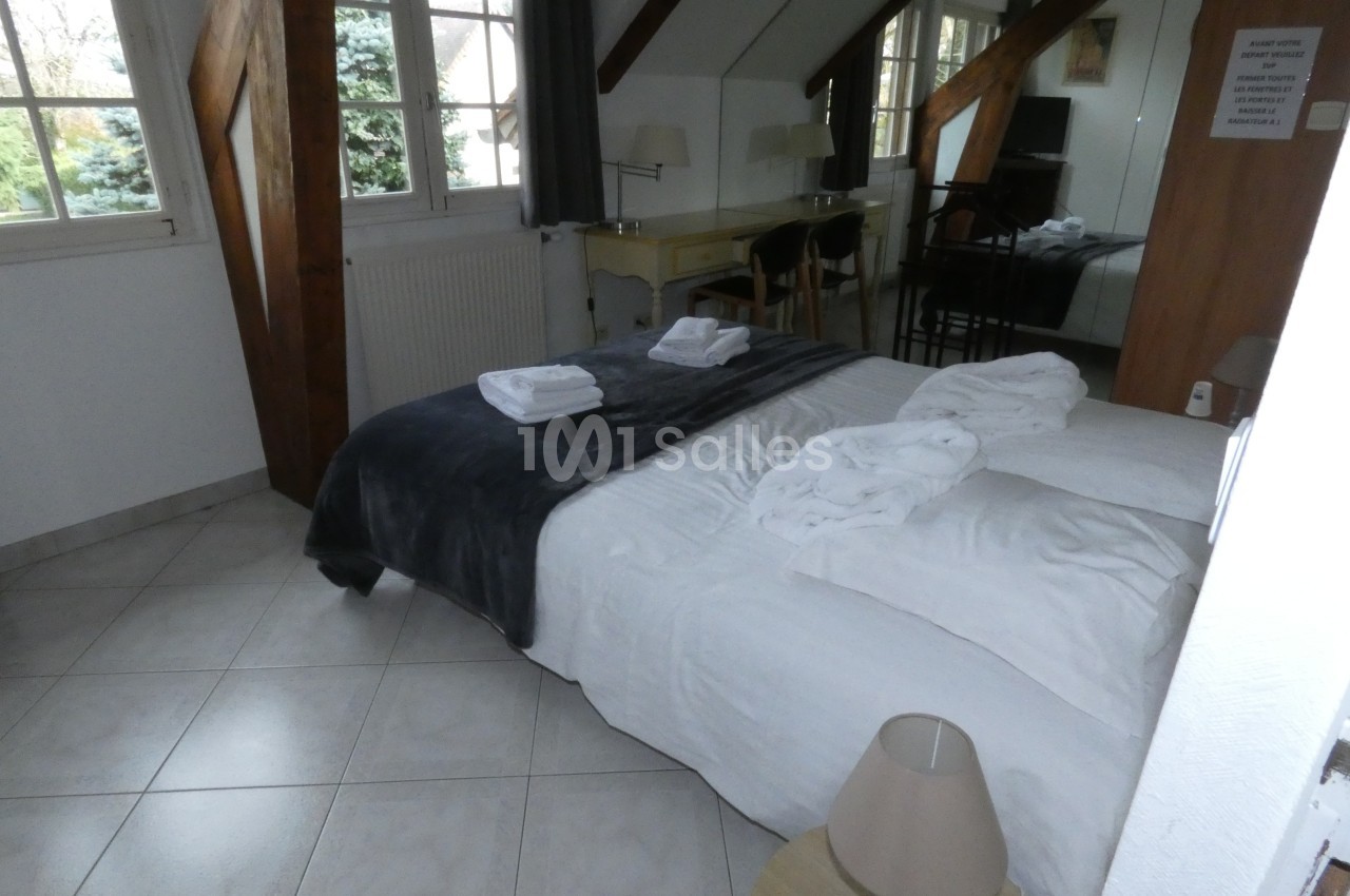 Chambre lumineuse avec lit double, draps blancs, peignoirs pliés, bureau en bois et fenêtres donnant sur un jardin.