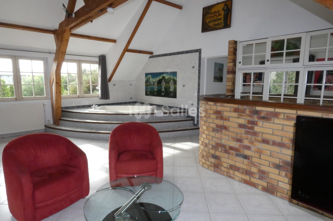 Salle lumineuse avec jacuzzi sur estrade, fauteuils rouges, table basse en verre et bar en briques.