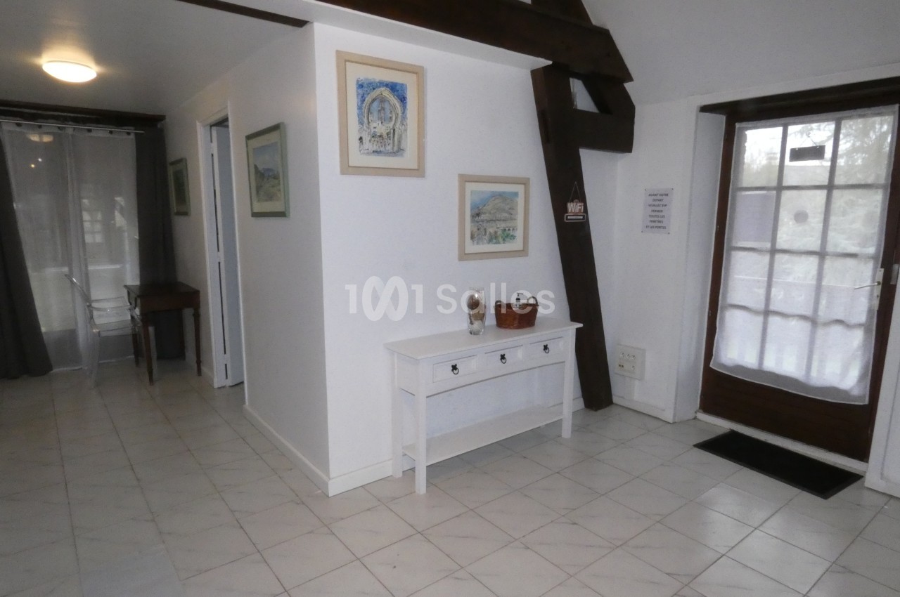 Entrée lumineuse avec sol en carrelage blanc, poutres apparentes, console blanche et porte-fenêtre vitrée.
