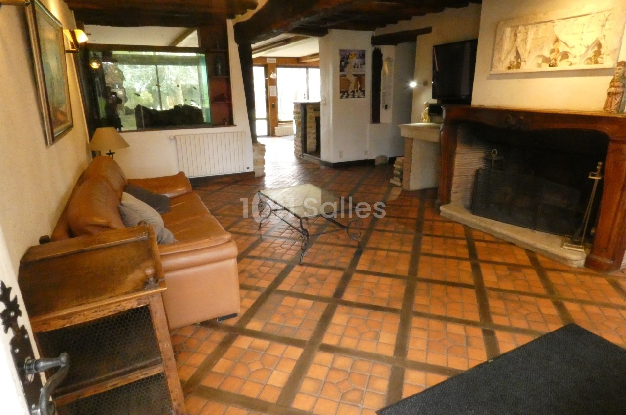 Salon rustique avec canapé en cuir, cheminée en pierre, poutres apparentes et sol en carreaux de terre cuite.