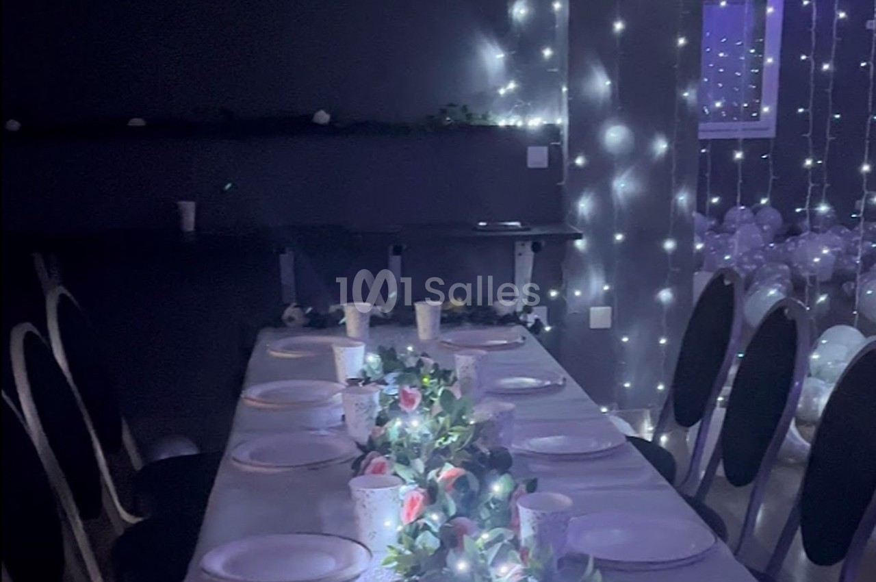 Table décorée avec une nappe blanche, guirlandes lumineuses, vaisselle et centre de table floral dans une salle sombre.