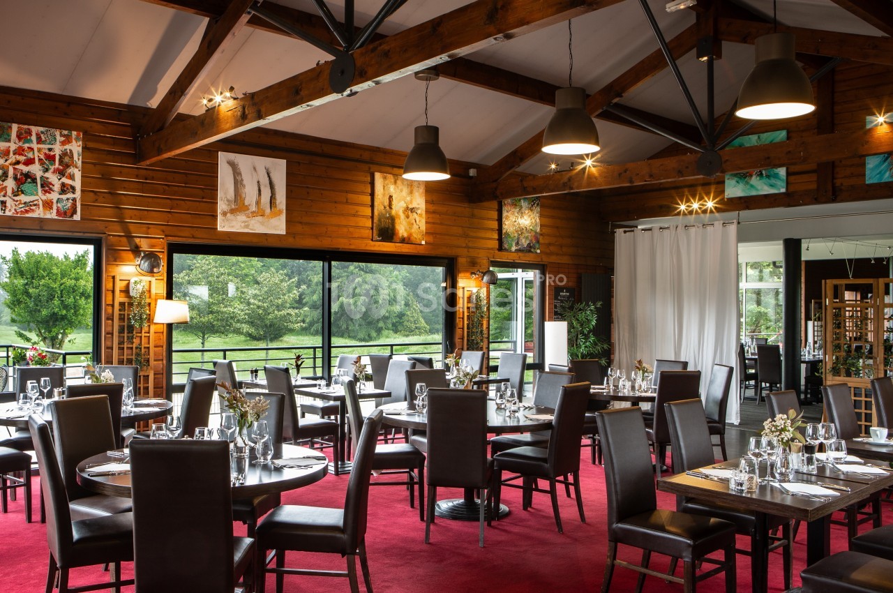 Salle de restaurant lumineuse avec tables dressées, chaises en cuir foncé, décorations murales et vue sur un jardin…