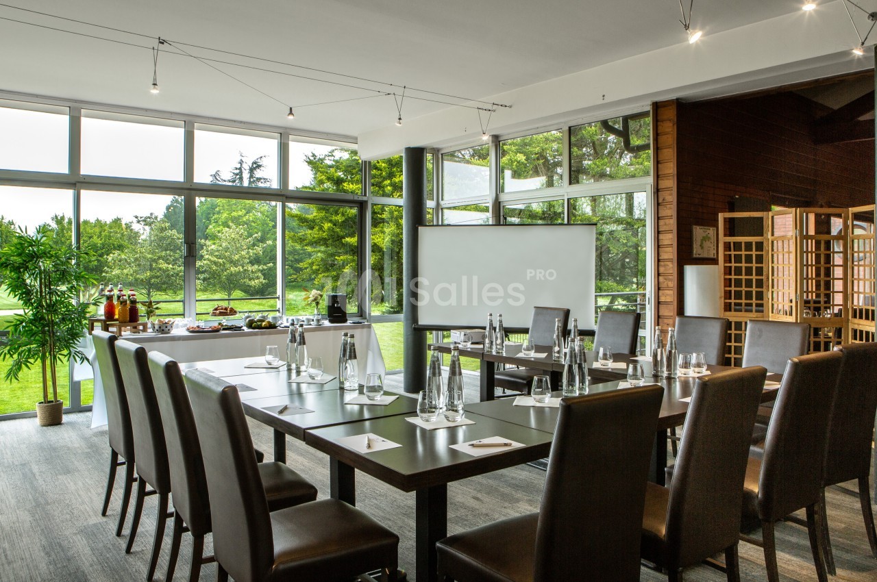 Salle de réunion lumineuse avec grandes baies vitrées, table disposée en U, et vue sur un espace vert extérieur.