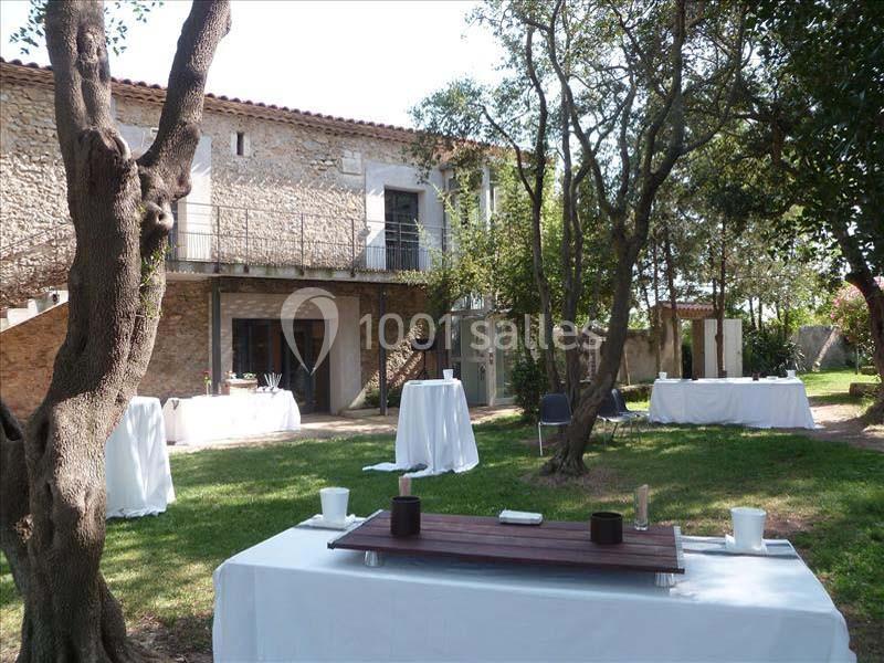 Espace extérieur avec tables dressées, arbres et bâtiment en pierre à l'arrière, ambiance calme et conviviale.