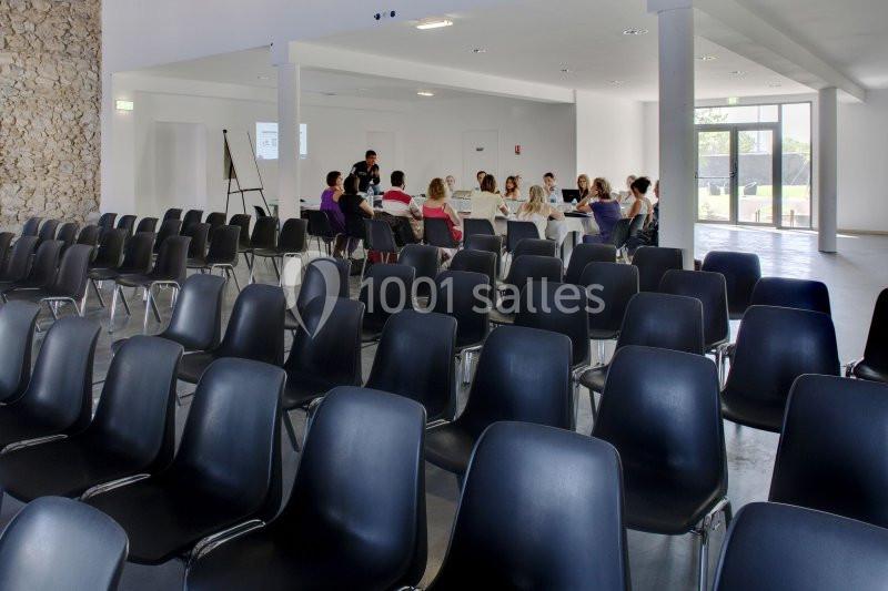 Des personnes assises autour d'une table dans une salle lumineuse, avec des rangées de chaises vides au premier plan.