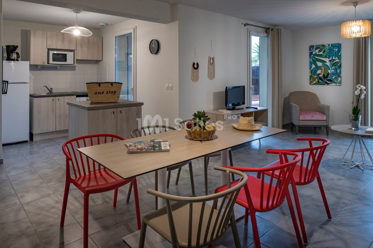Salle à manger et salon modernes avec table, chaises colorées, cuisine équipée et décoration chaleureuse.