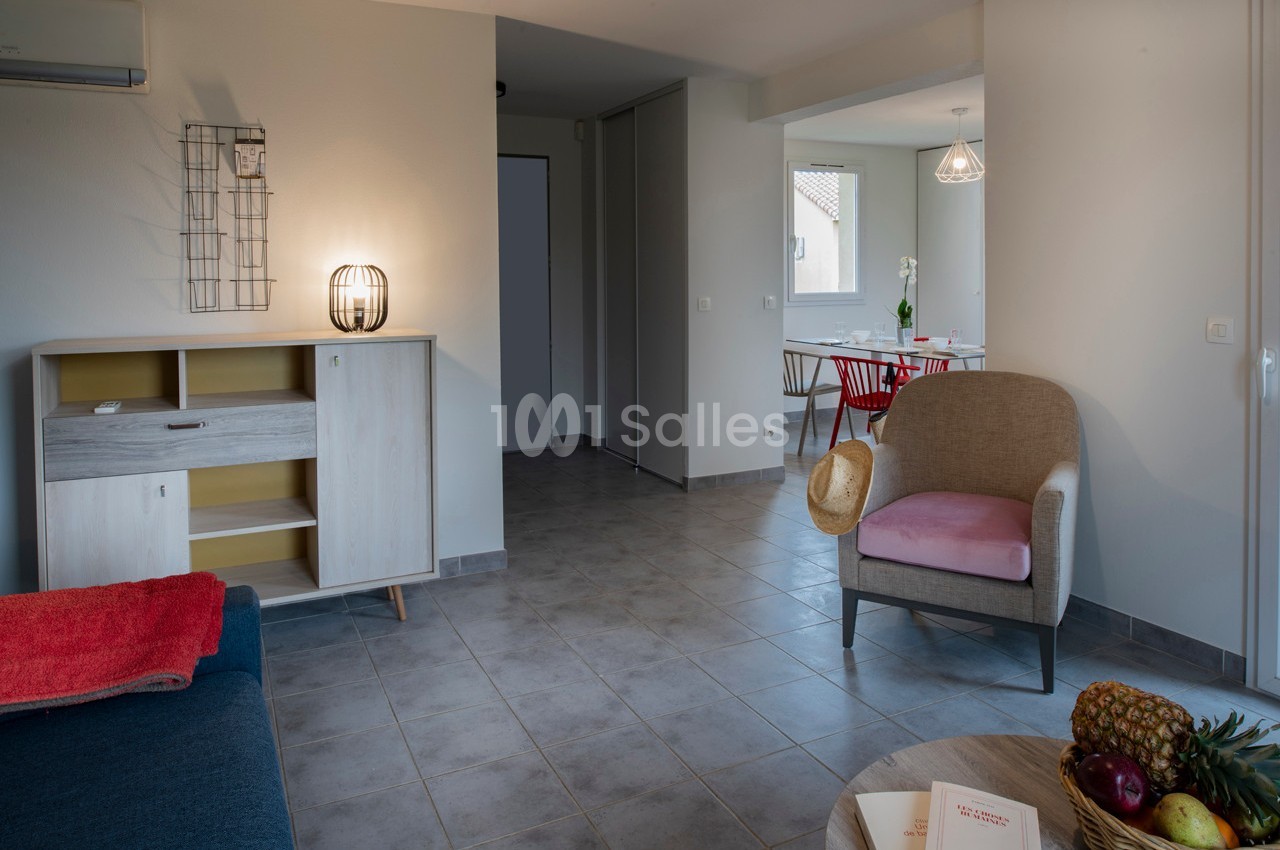 Salon lumineux avec mobilier moderne, fauteuil beige, table à manger et décoration minimaliste sur carrelage gris.