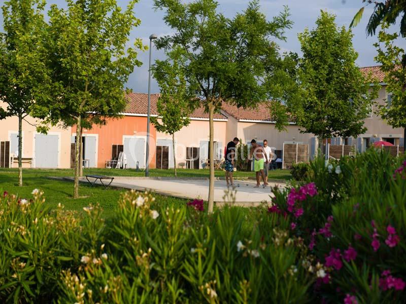 Des personnes marchent sur une allée bordée d'arbres et de fleurs, devant des bâtiments aux façades colorées.