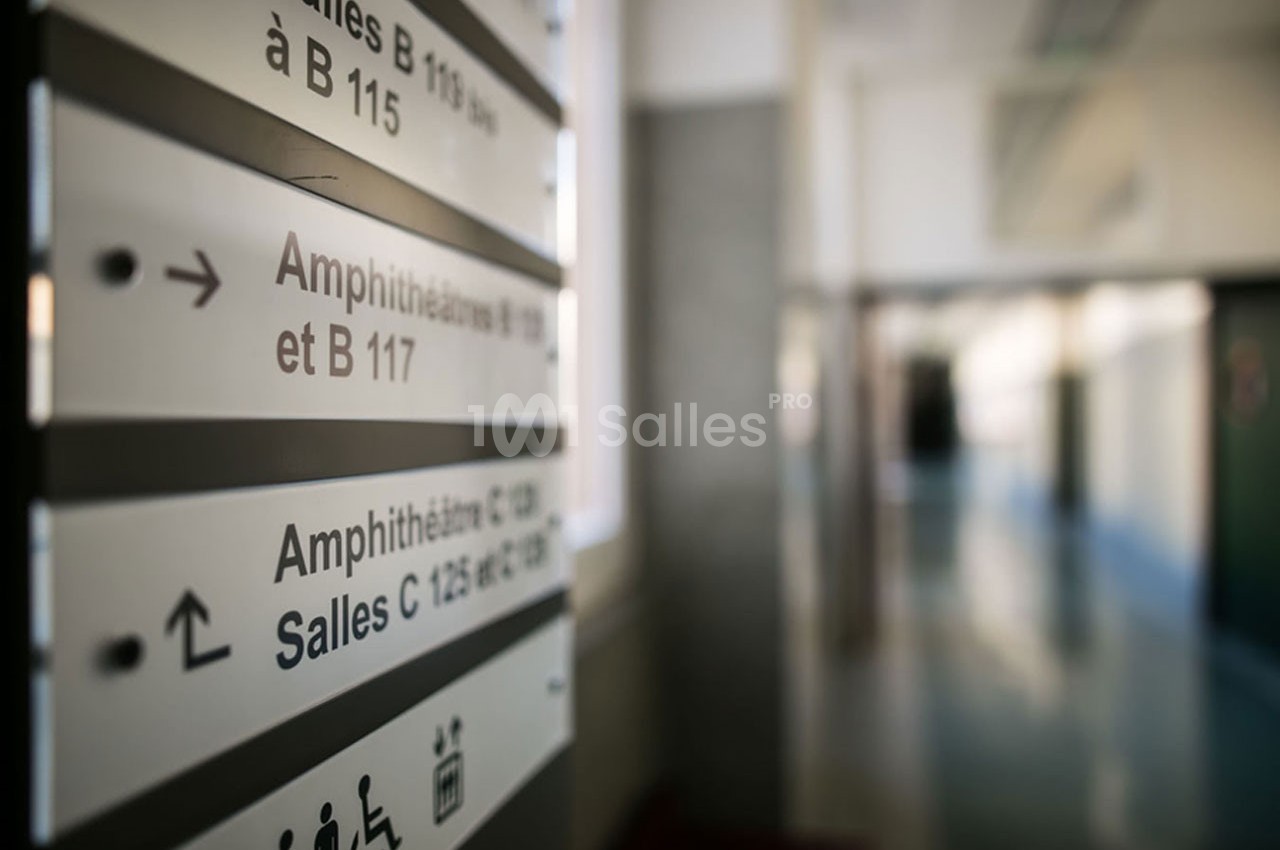 Panneau d'orientation dans un couloir indiquant les directions vers des amphithéâtres et des salles de cours.