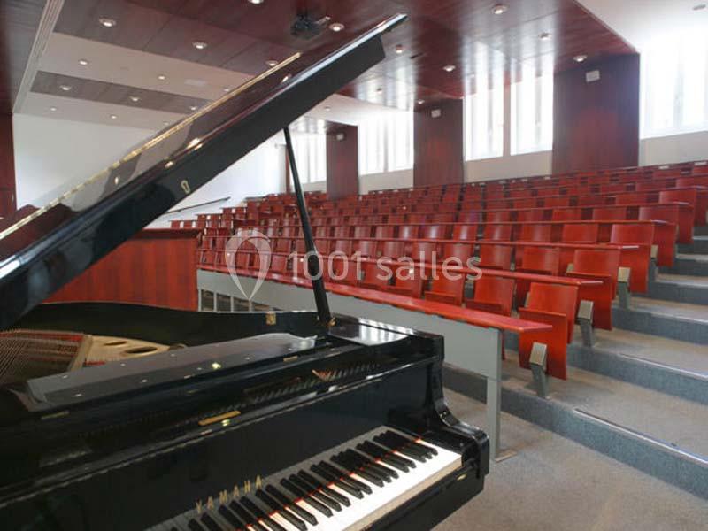 Un piano à queue noir dans une salle de conférence avec des rangées de sièges en bois vides.
