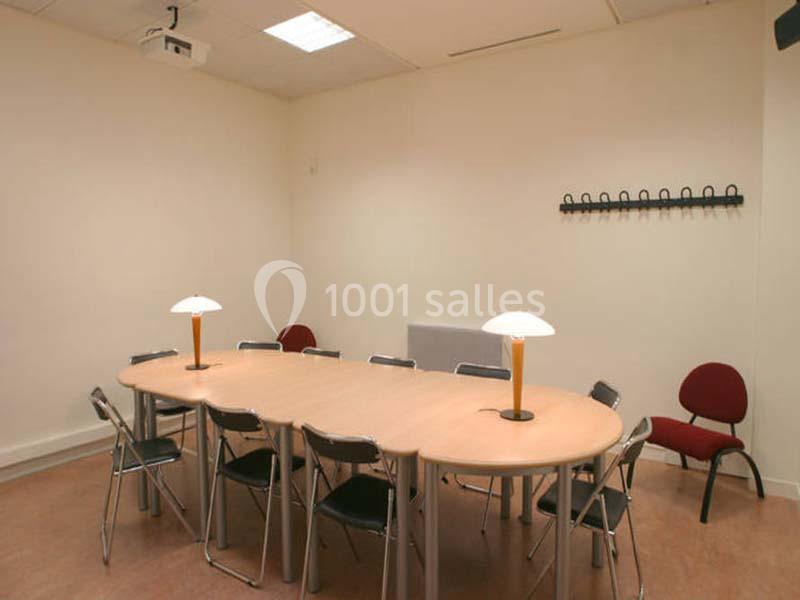 Salle de réunion avec une grande table ovale, des chaises, deux lampes allumées et un porte-manteau mural.
