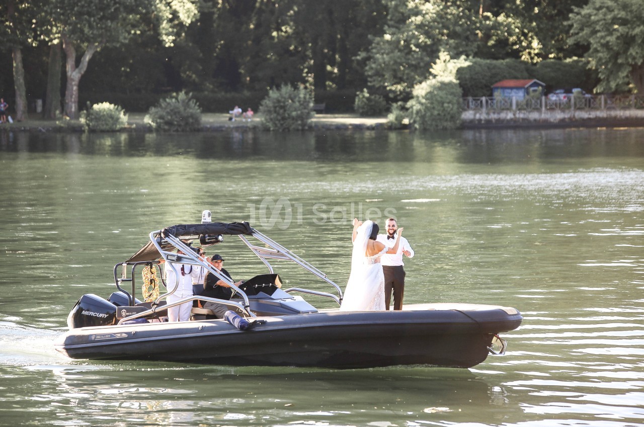 Un couple en tenue de mariage se tient sur un bateau à moteur naviguant sur un lac entouré de végétation.