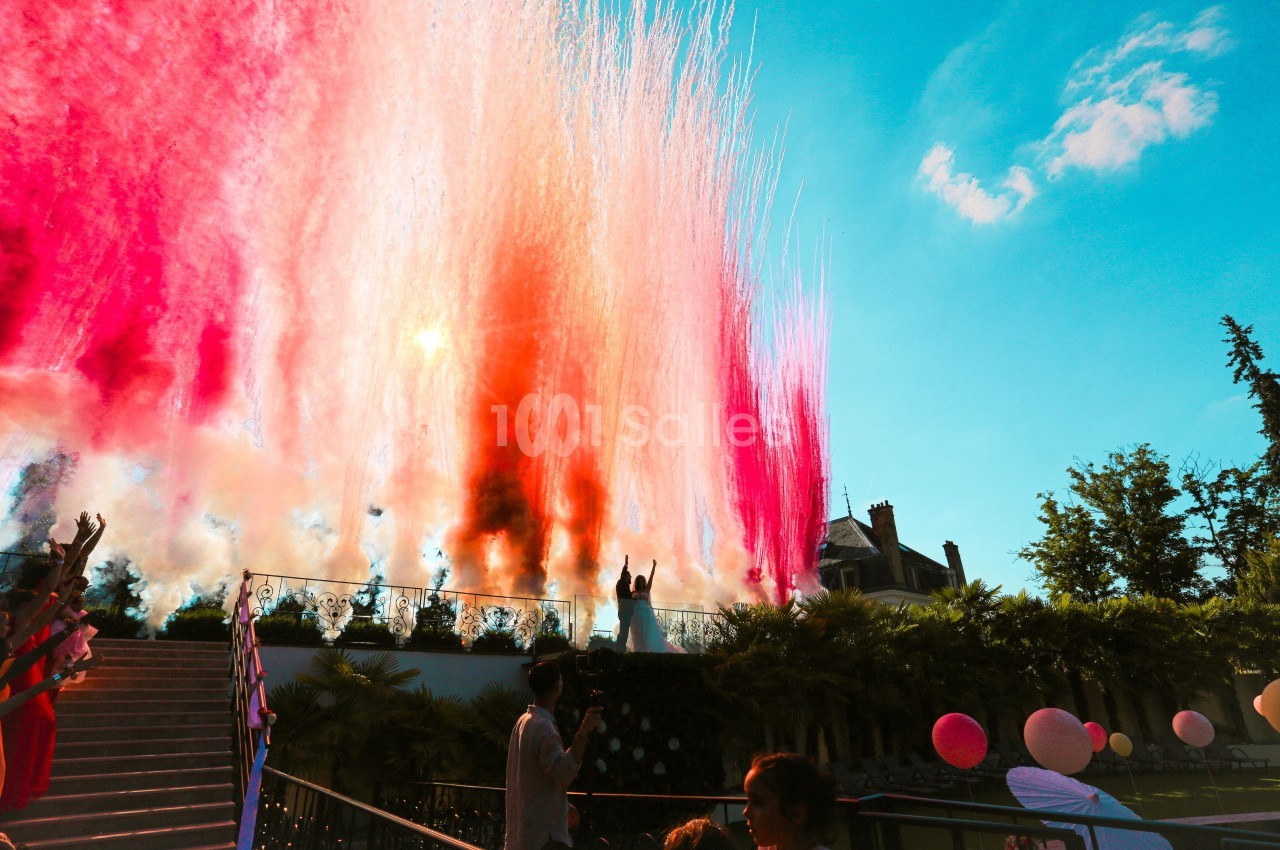 Jets de poudre colorée rose et orange projetés en l'air lors d'un événement en extérieur par temps ensoleillé.