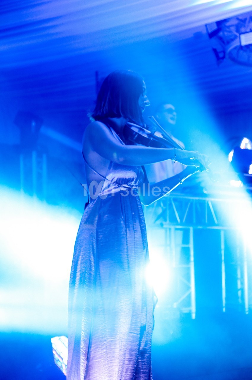 Une musicienne joue du violon sur scène sous des lumières bleues intenses.