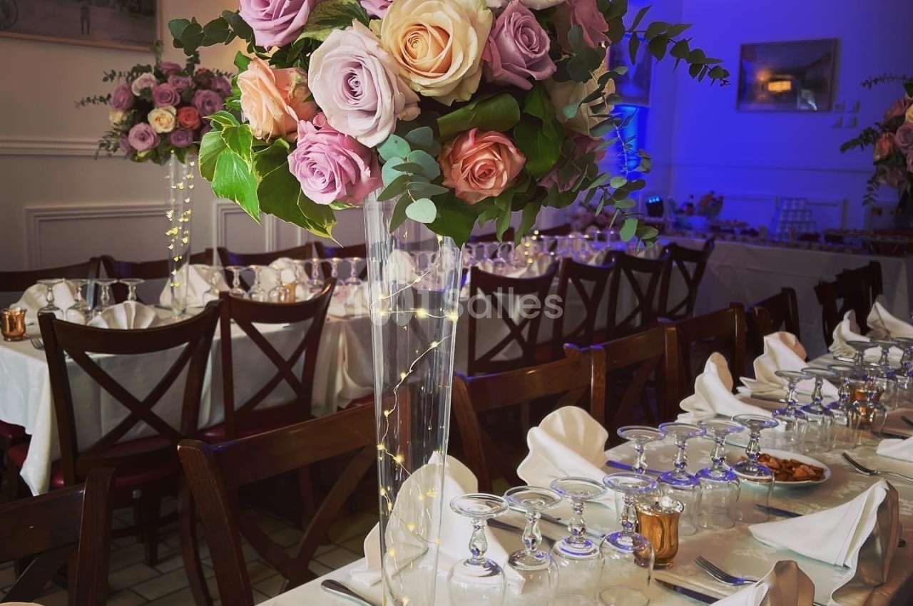 Centre de table floral avec roses pastel et feuillage, posé sur une table dressée pour un repas festif.