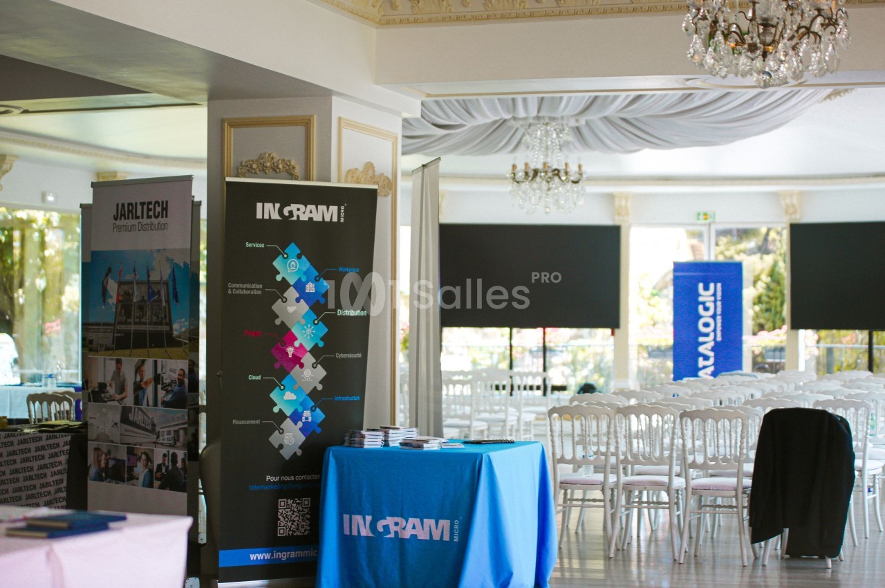 Salle lumineuse avec des stands promotionnels, des chaises blanches alignées et des affiches d'entreprises exposées.