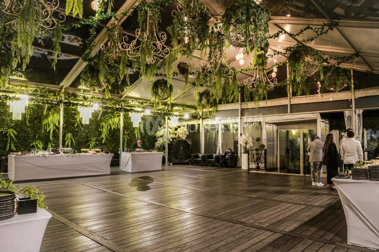 Salle de réception avec parquet en bois, décoration végétale suspendue et tables de buffet éclairées.