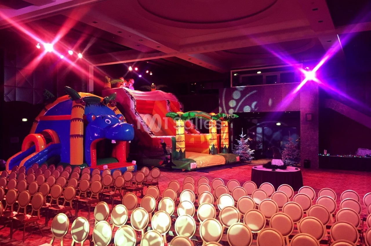 Deux structures gonflables colorées dans une salle de réception éclairée, avec des rangées de chaises vides au premier plan.