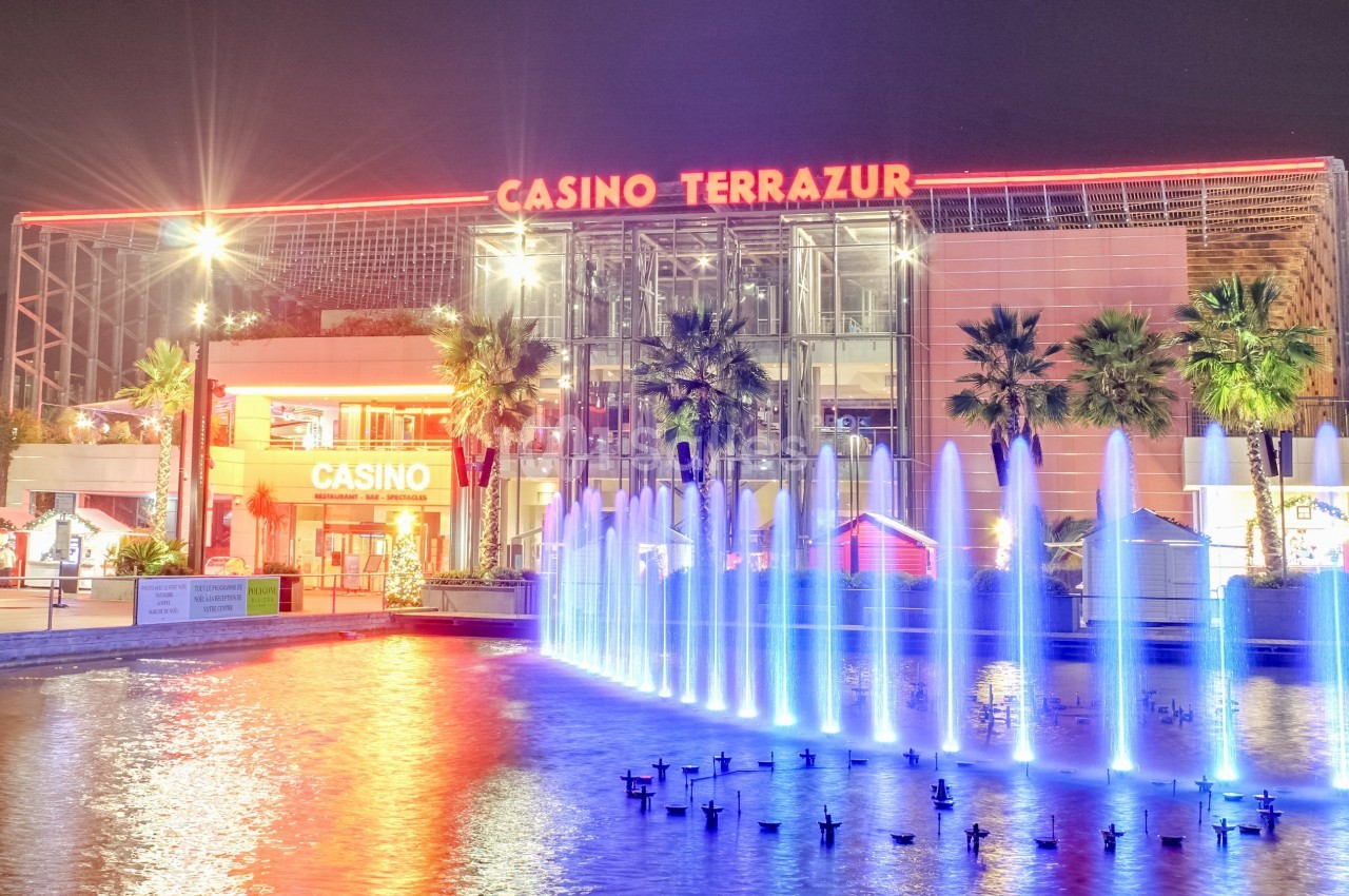 Façade illuminée du Casino Terrazur avec des jets d'eau colorés au premier plan, de nuit.