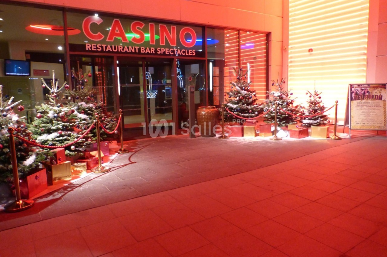 Entrée d'un casino décorée pour Noël avec des sapins illuminés et des cadeaux disposés devant la façade.