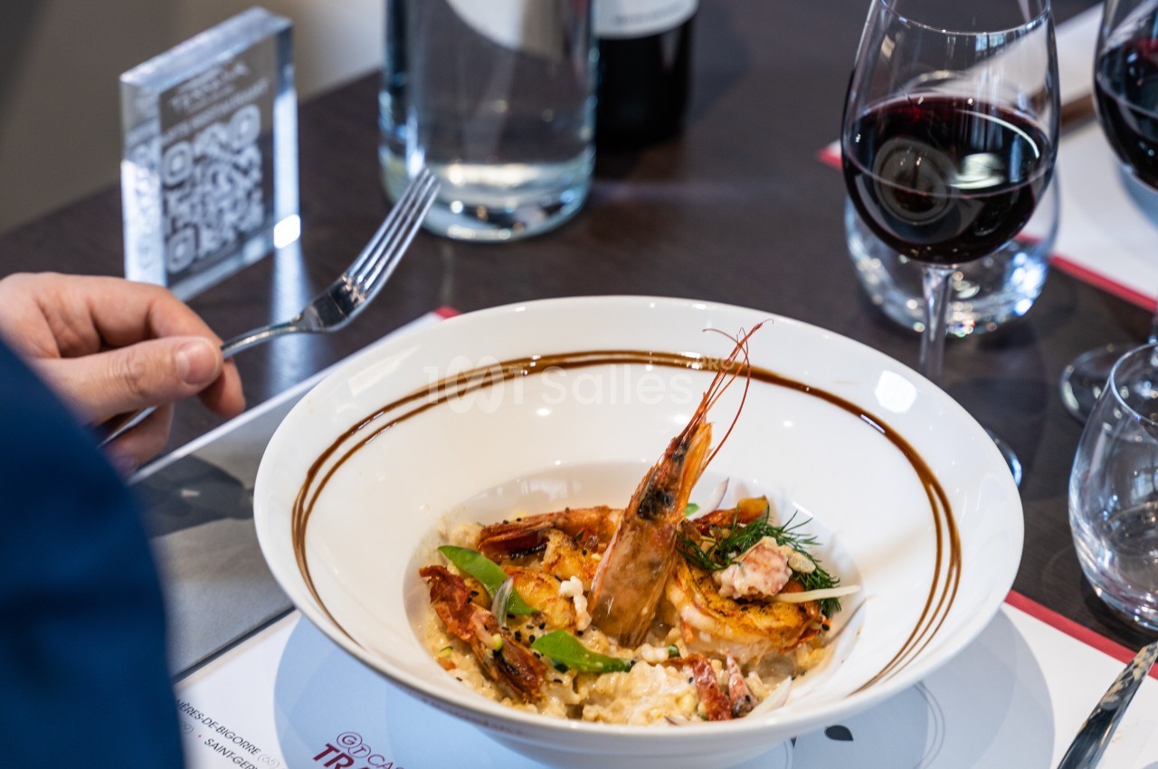 Assiette de risotto aux fruits de mer avec une crevette entière, servie sur une table avec des verres de vin rouge.