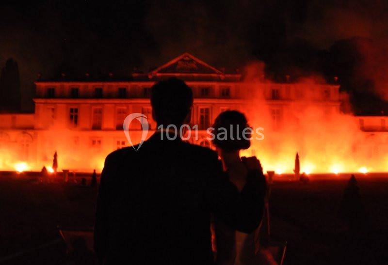Un couple de dos observe un bâtiment illuminé par des flammes ou des lumières intenses dans la nuit.