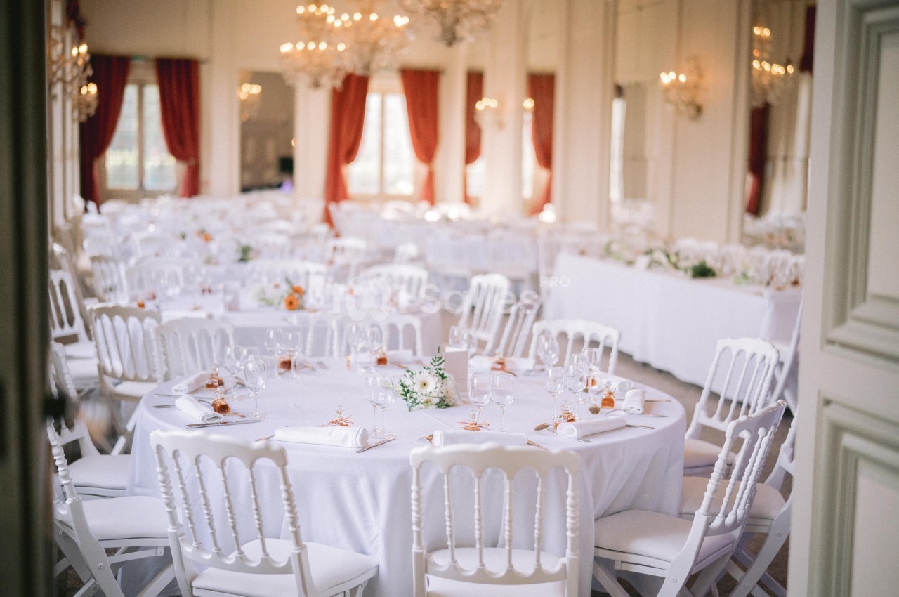 Salle de réception élégante avec des tables rondes dressées, nappes blanches et décorations florales.