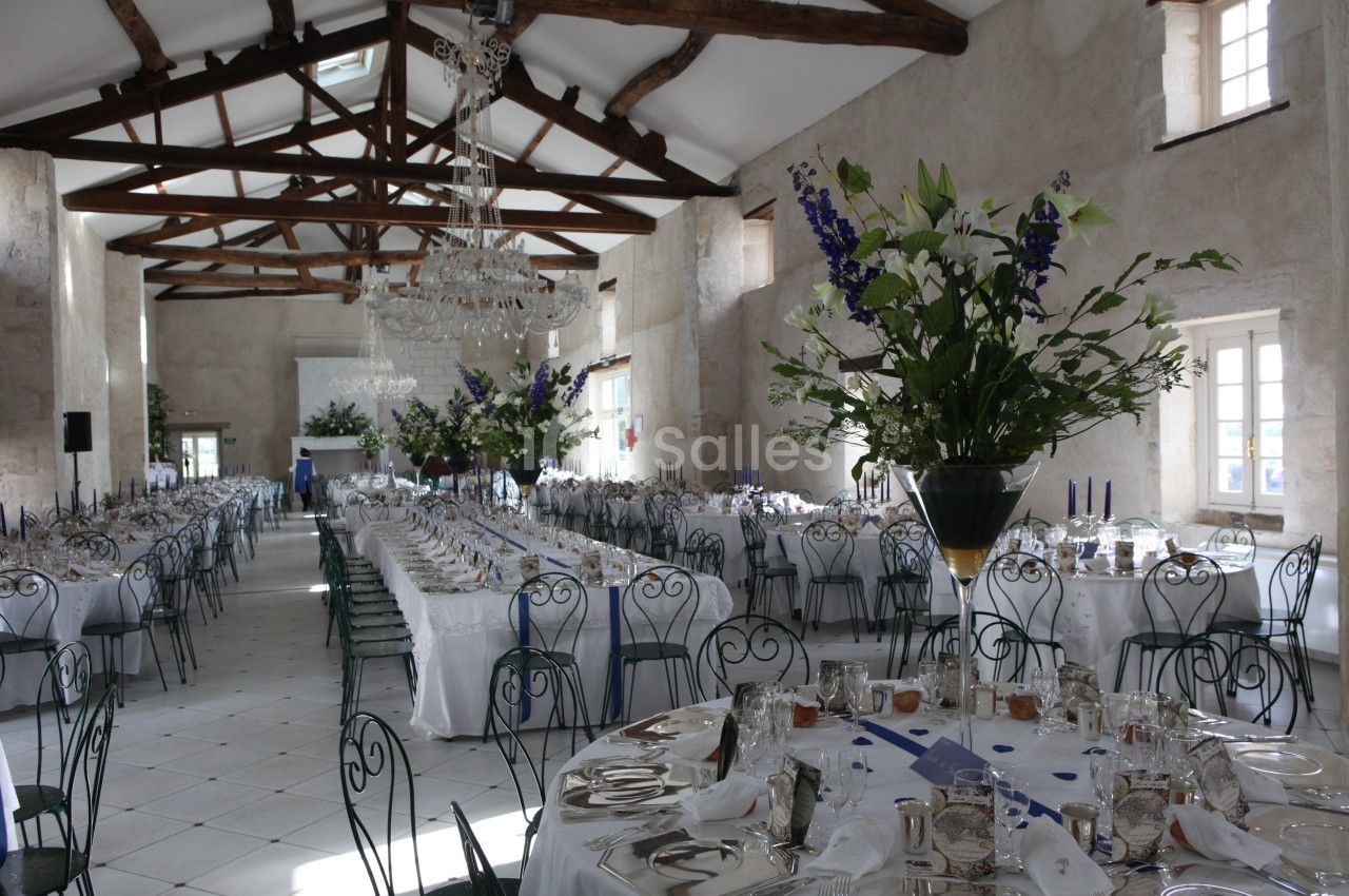 Grande salle de réception lumineuse avec tables dressées, chaises en fer forgé et décorations florales élégantes.