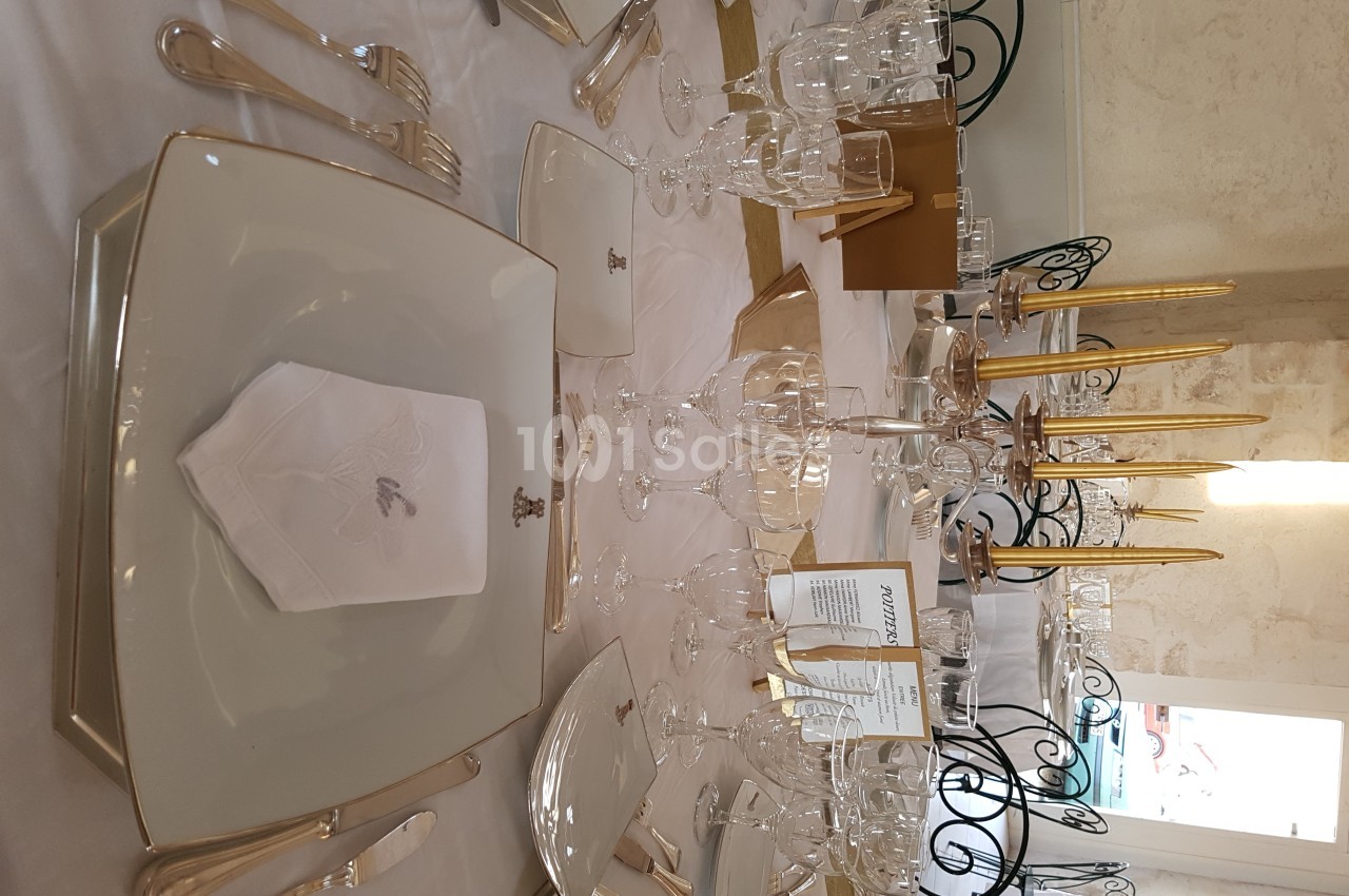 Table élégamment dressée avec assiettes carrées, serviettes pliées, verres à pied et bougeoirs dorés.