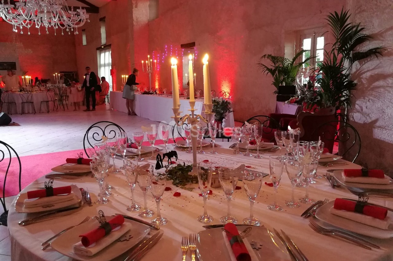 Table élégamment dressée dans une salle de réception décorée de chandeliers, lumières rouges et plantes.