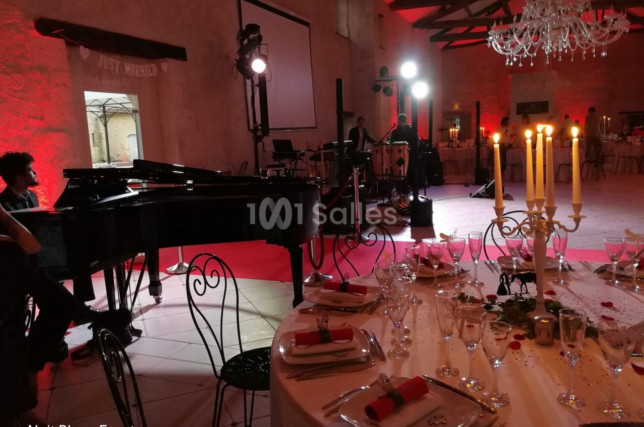 Salle de réception décorée avec chandeliers, piano à queue et éclairage rouge, prête pour un événement festif.