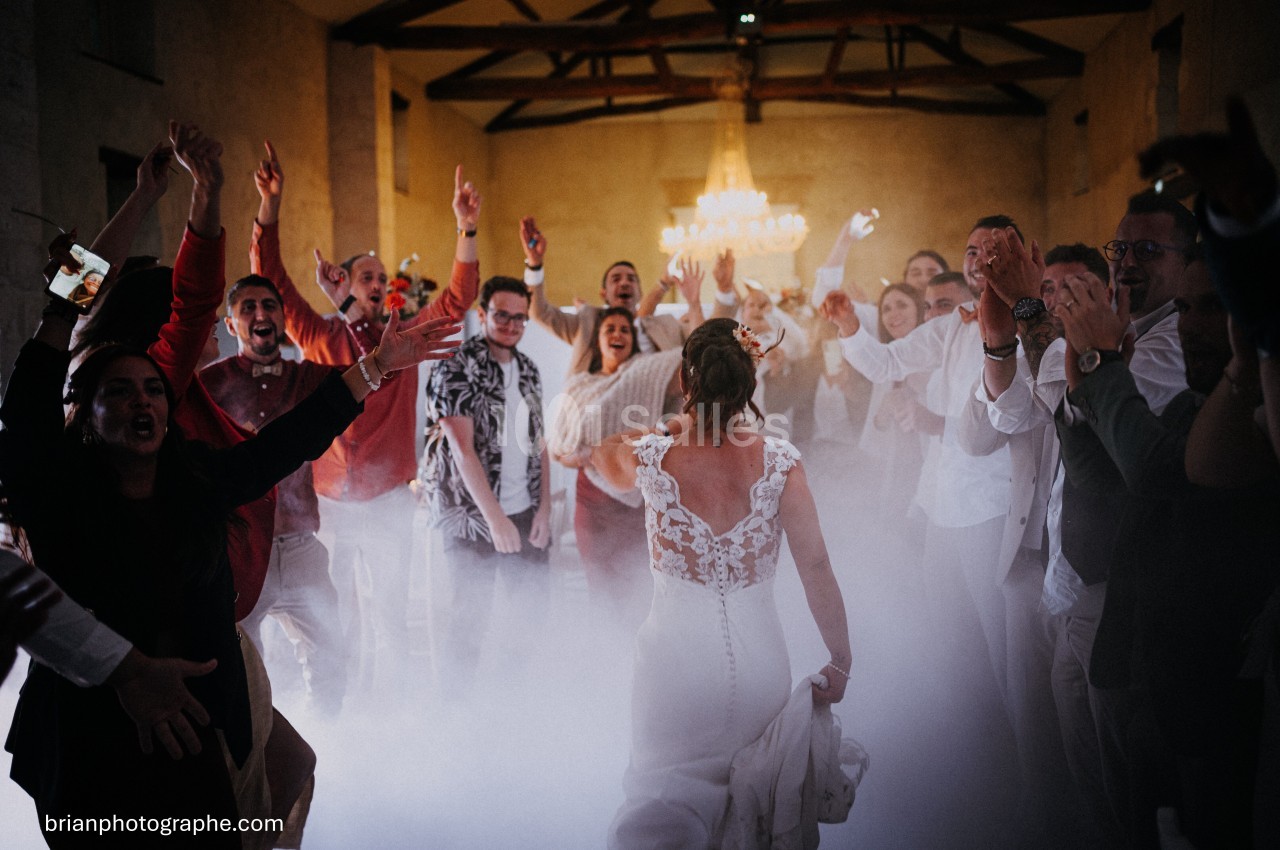 Une mariée en robe blanche danse au centre d'une salle entourée d'invités enthousiastes sous un éclairage chaleureux.