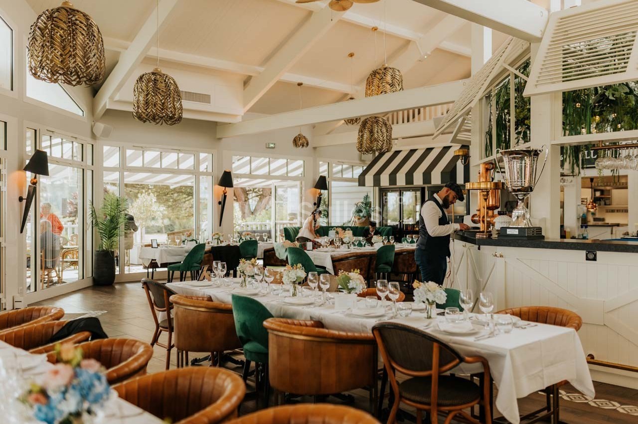 Salle de restaurant lumineuse avec tables dressées, chaises élégantes et décoration végétale et contemporaine.